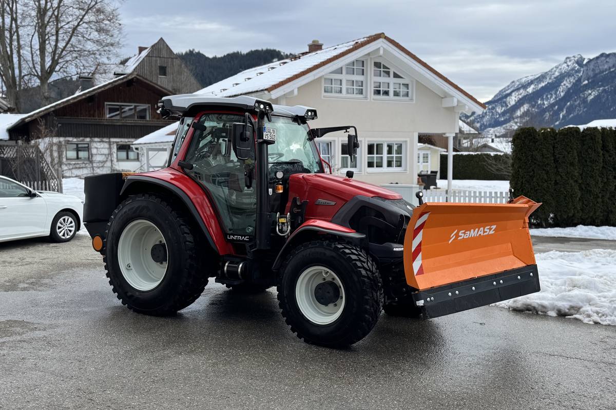 Traktor mit orangem Räumschild von Schmölz Hausmeisterservice auf einer geräumten Dorfstraße